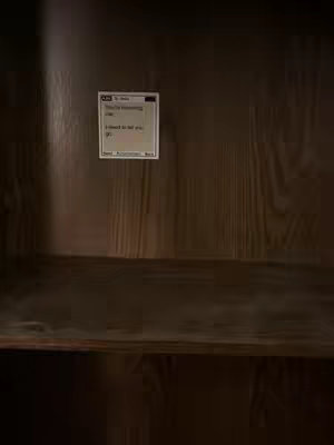 A medium shot shows a wooden structure. There's a shelf and a piece of paper stuck to it. The paper has text on it that looks like a text message.