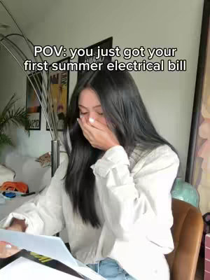 A woman with long black hair is shown with her hand over her mouth in apparent shock while holding a bill. Overlay text indicates that the bill is her first summer electrical bill.