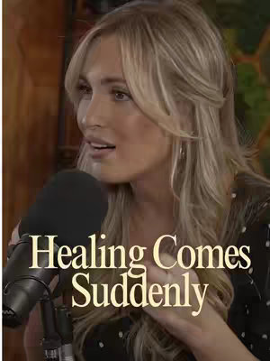 A woman with blonde hair is speaking into a microphone. Text overlayed on the image reads "Healing Comes Suddenly". The background is blurred, with warm, muted tones.