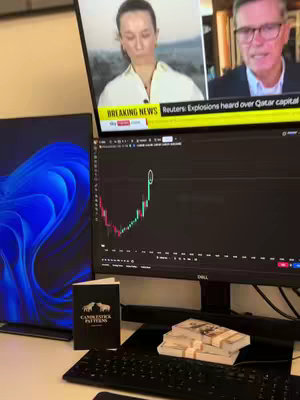 A workspace includes multiple monitors displaying news and a stock chart, along with a keyboard, a book labeled 'Candlestick Patterns,' and a stack of cash. The scene is well-lit, suggesting an office setup, with the focus on financial tools and data analysis.