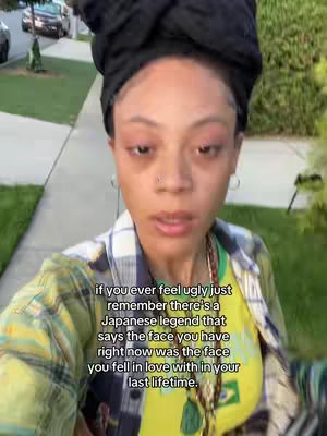 A selfie-style shot featuring a woman standing outside. She is wearing a colorful shawl, and a black head covering. The background includes a sidewalk, grass, and cars. On the bottom area, it has text overlay.