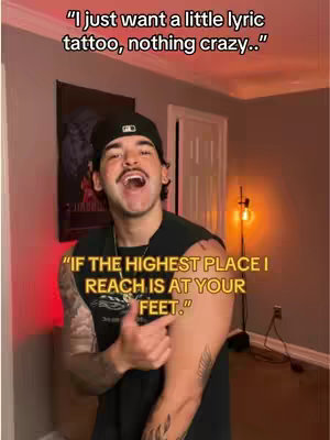 A man with a mustache is in a well-lit living room. He's smiling and gesturing towards his arm, which has a tattoo on it. Text overlays describe his desire for a lyric tattoo and a quote about reaching a higher place.