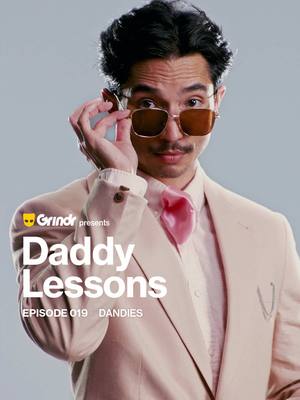 A man with dark hair and a mustache is wearing a light pink suit, a pink bow tie, and sunglasses. He is touching his sunglasses with his right hand. Written on the image is "Daddy Lessons" with the Grindr logo.