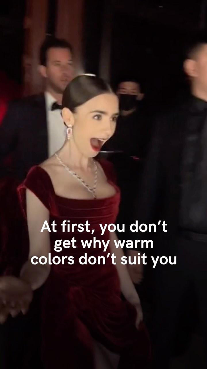 A candid shot of actress Lily Collins expressing surprise, wearing a dark red dress and jewelry, set against a blurred, dark background with onlookers. The text overlay reads 'At first, you don't get why warm colors don't suit you'.