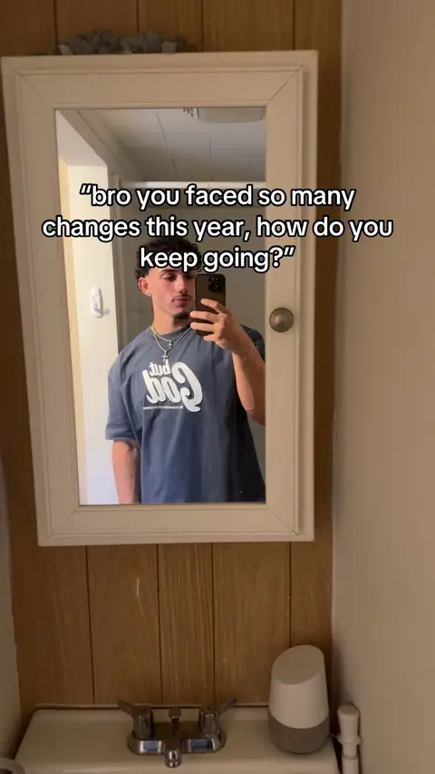 A man is shown in a bathroom mirror, holding a phone and taking a selfie. Text overlays the image, and he is wearing a casual t-shirt.