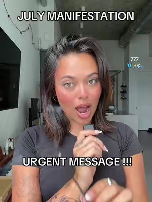 A woman with brown hair and fair skin is looking at the camera with an open mouth, possibly speaking. The backdrop is a lightly colored room with a window and a few visible decor elements. The image has two text overlays: "JULY MANIFESTATION" at the top and "URGENT MESSAGE !!!" at the bottom.