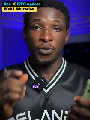 A man with dark skin and short hair is centered in the frame, looking directly at the camera. He wears a black vest with white stripes and a white collar, and a small microphone is attached to his shirt. The background is a gradient of blues. Text overlays are placed at the top of the frame. The composition focuses on the man's face and upper body.