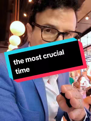A man in a blue blazer and glasses is the subject of the image. A text overlay in a black box with colored borders states, 'the most crucial time'. The background is out of focus, suggesting a public venue with warm lighting.