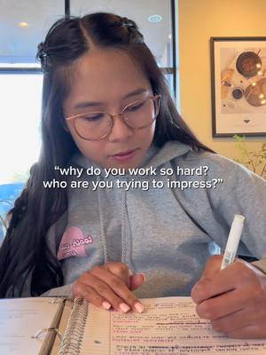 A young woman with long dark hair sits in front of a window, writing in a notebook. She wears glasses and a gray hoodie. Text overlays the image, posing a question.