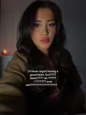 A medium shot shows a young woman with long, dark hair and a neutral expression, looking towards the camera. She's wearing a brown jacket, and the background is dimly lit, with a small candle to the left.