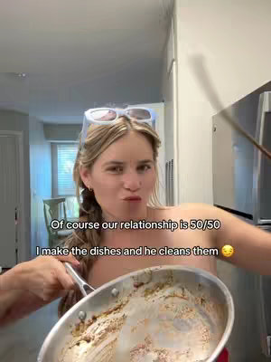 A woman with sunglasses on her head is looking at the camera and holding a dirty pan, suggesting a cooking or cleaning setting.