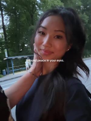 A young woman with long dark hair, seen from the chest up, is the central focus, softly smiling. She is in an outdoor setting with trees visible in the background. A short text overlay is positioned at the bottom.