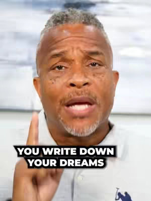 A medium shot of a man with short, graying hair pointing upwards with his index finger. The man has a serious expression, and the overlaid text reads, "YOU WRITE DOWN YOUR DREAMS."