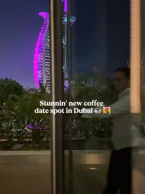 The cover image shows a nighttime cityscape reflected in a glass pane. The Burj Al Arab hotel, illuminated in pink and white lights, is prominently featured on the left side. A person is visible on the right side. Superimposed over the scene is text in a handwritten font, with emojis, inviting viewers to a 'new coffee date spot in Dubai'. The overall impression is sophisticated, hinting at an upscale destination.