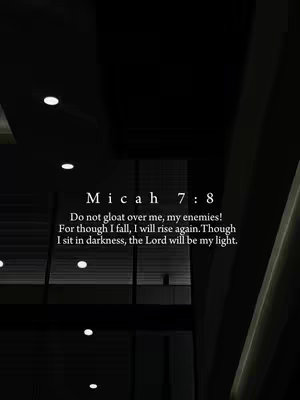 The image features a dark interior scene, possibly a building or hall, with an overhead view that is out of focus. The predominant color is black, with bright circular lights dotting the ceiling. In the center, a square text box displays a quote from Micah 7:8, using a clean, white font. The layout is simple and elegant, focusing attention on the biblical verse against the dark backdrop.