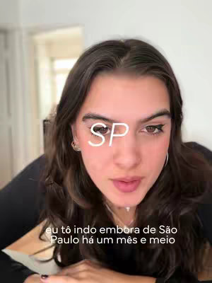 A person with long dark hair looks directly at the camera, with a white text overlay of 'SP' partially covering their face. The background is blurred, providing a soft focus on the individual.