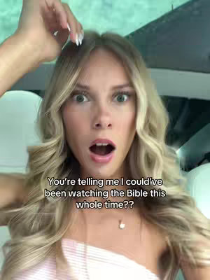 A young woman with long blonde hair stares at the camera with a surprised expression, mouth open. She has a light pink top, and a small necklace. Text overlay appears above the bottom center of the frame.