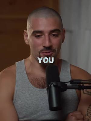 A man with a shaved head and a light gray tank top is in front of a black microphone. The word "YOU" is superimposed in white text over his chest. The lighting appears to be natural, and the background is out of focus.