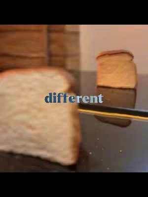 The cover image shows two slices of bread in focus, one larger and slightly blurred on the left, the other a smaller slice on a reflective surface. In the background, a blurred wooden surface is visible. An overlay of blue-tinted text reads "different". The composition uses a shallow depth of field to emphasize the bread.