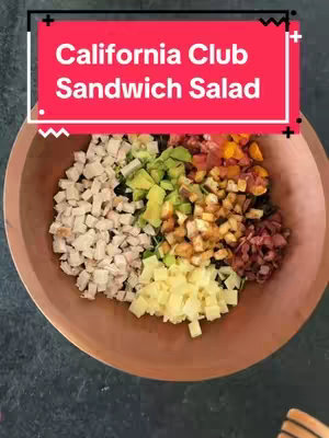 A top-down shot showcasing various ingredients of a California Club Sandwich Salad arranged in a wooden bowl. The ingredients, including diced turkey, avocado, tomatoes, bacon, and cheese, are neatly segmented, ready to be mixed.