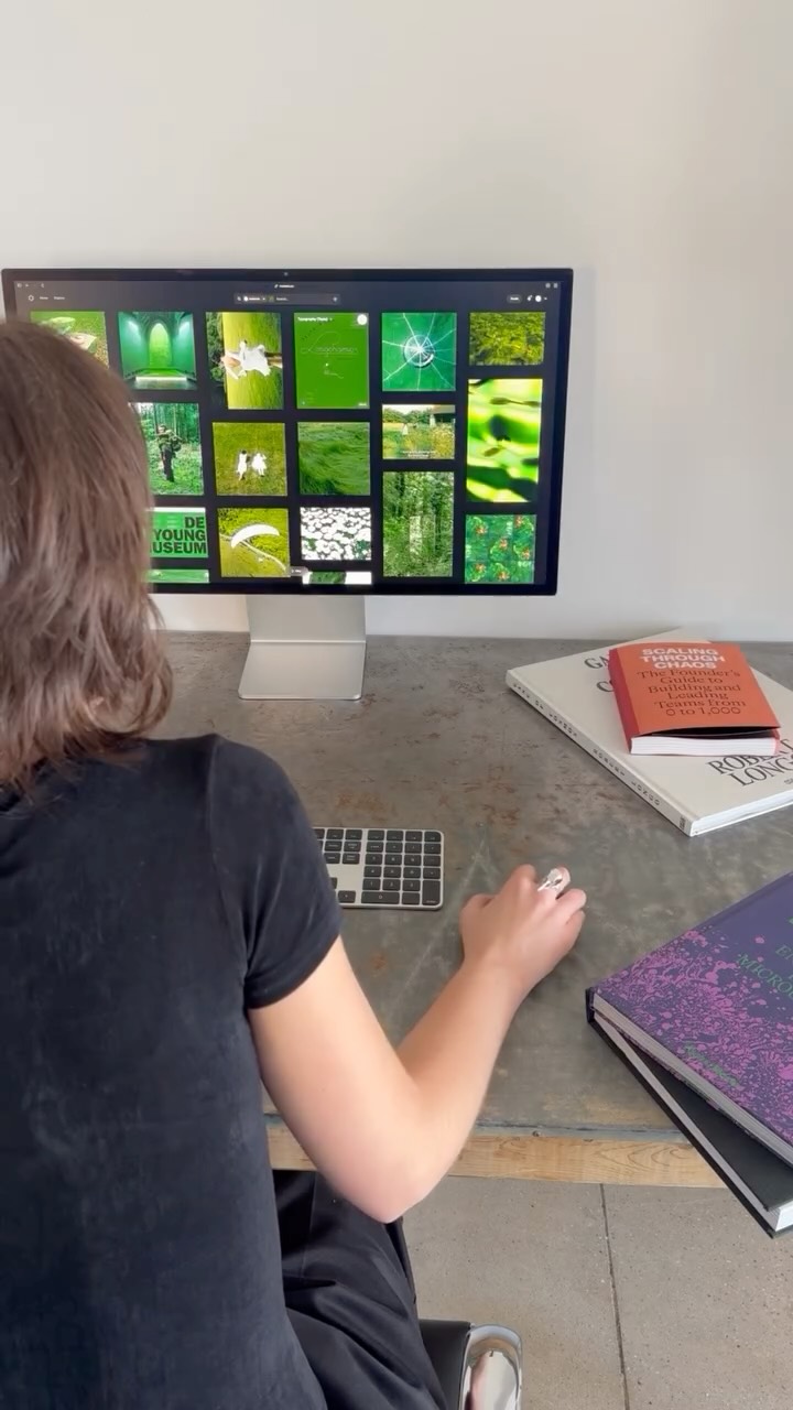 A person is shown from behind, sitting at a desk with a computer monitor displaying a set of green-toned images. Various books and a small keyboard are on the desk. The overall aesthetic is clean and modern with a focus on the color green.
