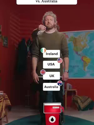 A man stands in front of a red background. On his chest is a rectangular list with country flags. At his feet is a red and white gas pump.