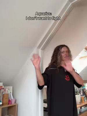 A person with curly hair gestures with open palms in what appears to be a home setting, next to a white wall and door trim. Text overlay reading 'Aquarius: I don't want to fight' is at the top.