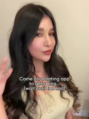 A woman with long dark hair, light skin, and neutral lip color is positioned slightly off-center. A text overlay is present at the bottom of the frame. The background is a plain, neutral wall.