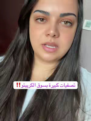 A woman with long dark hair and brown eyes looks towards the camera. She is wearing a white top. A text overlay in white letters with a purple background says, "تصفيات كبيرة بسوق الكريبتو!!" (Big liquidations in the crypto market!!).