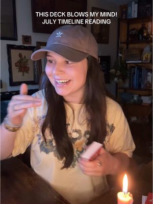 The cover image features a woman with long dark hair, wearing a brown cap and a light yellow t-shirt. The woman sits at a dark wooden table in a dimly lit room with antique-style aesthetic, holding a deck of cards, and gesturing with her left hand. To her right is a candle. Overlaying the image at the top is white text. The composition is warm and inviting.