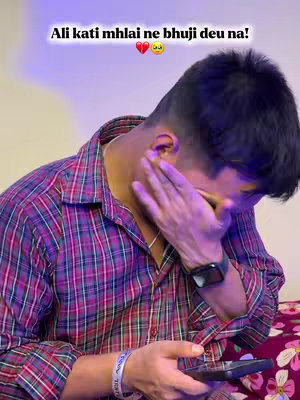 A young man is shown in the image, seen from the chest up. He's wearing a red and black plaid shirt that's partially unbuttoned, revealing a bit of his chest. His left hand is up near his face, partially covering his eyes, which suggests he might be emotional or distressed. He is holding a phone in his other hand. Overlayed on the top, there's text over the image, adding context. The lighting seems to be soft and purplish, which could be from an artificial source.