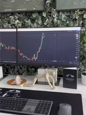 A setup with multiple computer monitors displaying financial charts and data. Additional elements include a model of a person, a keyboard, mouse, and some books on the desk.