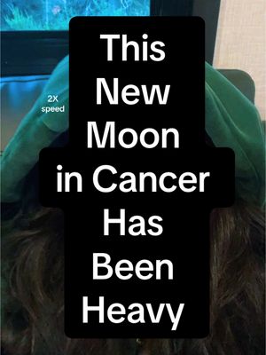 The image is a vertical video cover featuring a black rectangle with white text overlaid on top of a person's hair and a green hoodie. The text reads: “This New Moon in Cancer Has Been Heavy”. A small box in the top left corner says “2x speed”.