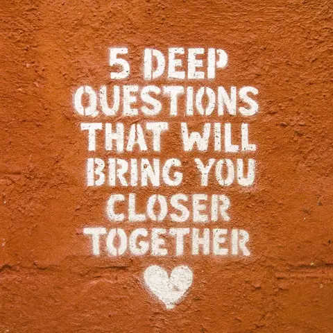 An orange brick wall with white stenciled text reading "5 DEEP QUESTIONS THAT WILL BRING YOU CLOSER TOGETHER" with a white heart at the bottom.