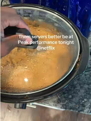 A close-up shot of a slow cooker with a glass lid, containing a creamy orange dish. The image is taken from a slightly above angle. A black-handled lid is at the top of the scene. A hand is holding the lid. The text overlay reads, 'Them servers better be at peak performance tonight @netflix.' The focus is slightly soft.