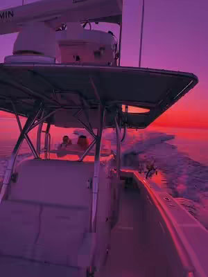 The image shows a boat moving on the water, viewed from inside. The camera angle is from the side of the boat, looking towards the bow and the horizon. The lighting is dim, mostly in shades of purple, with a bright red-orange sky.