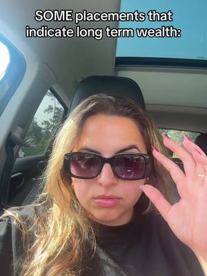 A woman wearing sunglasses inside a car is the main focus. Text overlays at the top of the image read: "SOME placements that indicate long term wealth:" The image is shot from a slightly low angle.