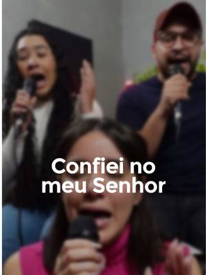 A blurry, close-up image shows three people singing into microphones. Text overlayed on the image reads, "Confiei no meu Senhor", set in white font.