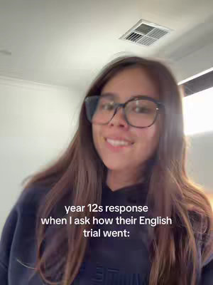 A young woman wearing glasses smiles at the camera from a low angle. Her brown hair is long and falls to her shoulders. She is wearing a black hoodie. At the bottom of the image, there is white text.