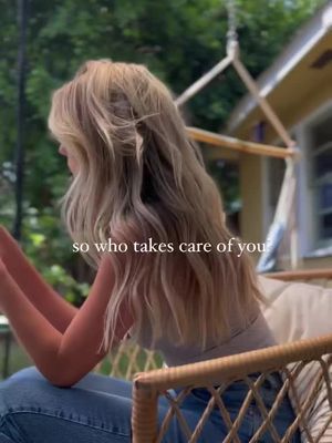 A person with long blonde hair, seen from the back, is seated on a wicker chair, partially obscuring a natural outdoor background. Text overlay reads: 'so who takes care of you'.