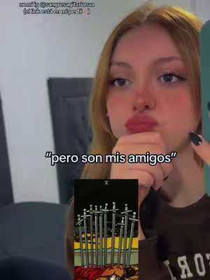 A young woman with long blonde hair holds a smartphone in front of her face, her expression is slightly puckered. Text overlays are present at the top and bottom of the frame. A tarot card is displayed at the bottom.