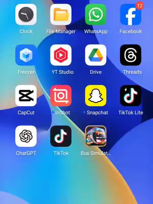 A mobile phone screen is displayed, showing a collection of app icons arranged in a grid against a blurred blue background. Dominant apps include those for social media (Facebook, TikTok, Snapchat), content creation (YT Studio, CapCut, InShot), communication (WhatsApp), and various utilities (Clock, File Manager, ChatGPT, Bus Simulator). An unread message count of '12' is visible on the Facebook app icon.
