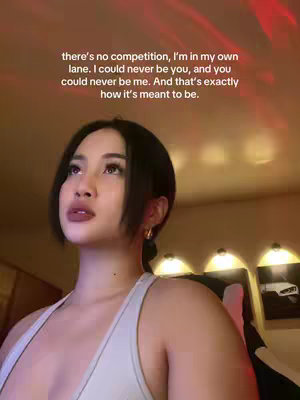 A young woman with dark hair and gold hoop earrings looks upwards, framed from the chest up. The background is a warm, blurry mix of orange and red hues from the lighting. Text in a white sans-serif font overlays the image.