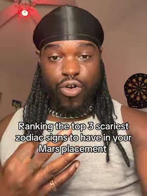 A selfie-style shot of a Black man with long, braided hair and a durag. The background is a room with a ceiling fan and a partially visible dartboard. Text overlays the image, providing context. The man has a nose ring and is wearing a chain. His hand is up, and he appears to be speaking.