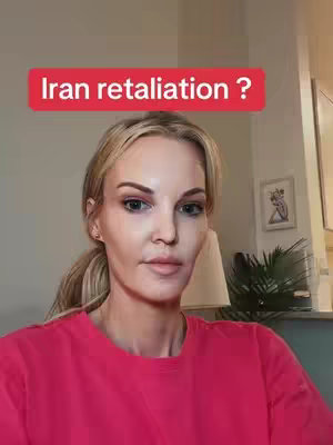 A medium shot features a fair-skinned woman with blonde hair pulled back in a ponytail, set against a neutral background. She's wearing a bright pink top, and the focus is on her face. Over her head is a red rectangular text overlay that reads, "Iran retaliation ?" The background shows a glimpse of a home interior, with a lamp and what appears to be a framed picture or artwork that suggests it's a living room or similar indoor space.