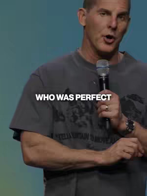 A man wearing a grey t-shirt with a microphone in hand stands in front of a blue-green background, with the text 'WHO WAS PERFECT' overlaid on the image.