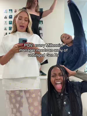 A group of four women in an office setting. The primary focus is on a blonde woman in white and floral pants looking at her phone, appearing to speak as three other women in the background react emphatically. The text overlay reads "POV: every Millennial manager needs an army of unhinged Gen Zs". The composition is dynamic, with movement and expressions capturing a humorous, relatable office moment.