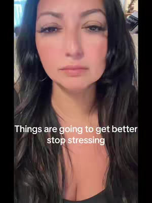 A medium shot of a woman with dark hair looking towards the camera with a neutral facial expression. She has makeup on, the lighting is soft, and text overlay in white which reads, "Things are going to get better stop stressing".