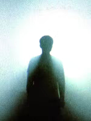 The image features a silhouette of a person standing in front of a bright, white light. The figure's form is dark, suggesting a shadow effect against the glowing background. The composition is simple, with the person centered and the light filling the rest of the space, creating a dramatic and ethereal feel.