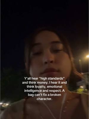 A selfie-style shot in a dark outdoor setting, where a woman is positioned in the center, looking towards the camera. Text overlay, written in white, is featured at the bottom half of the frame; the background appears blurry, with some visible lights. 